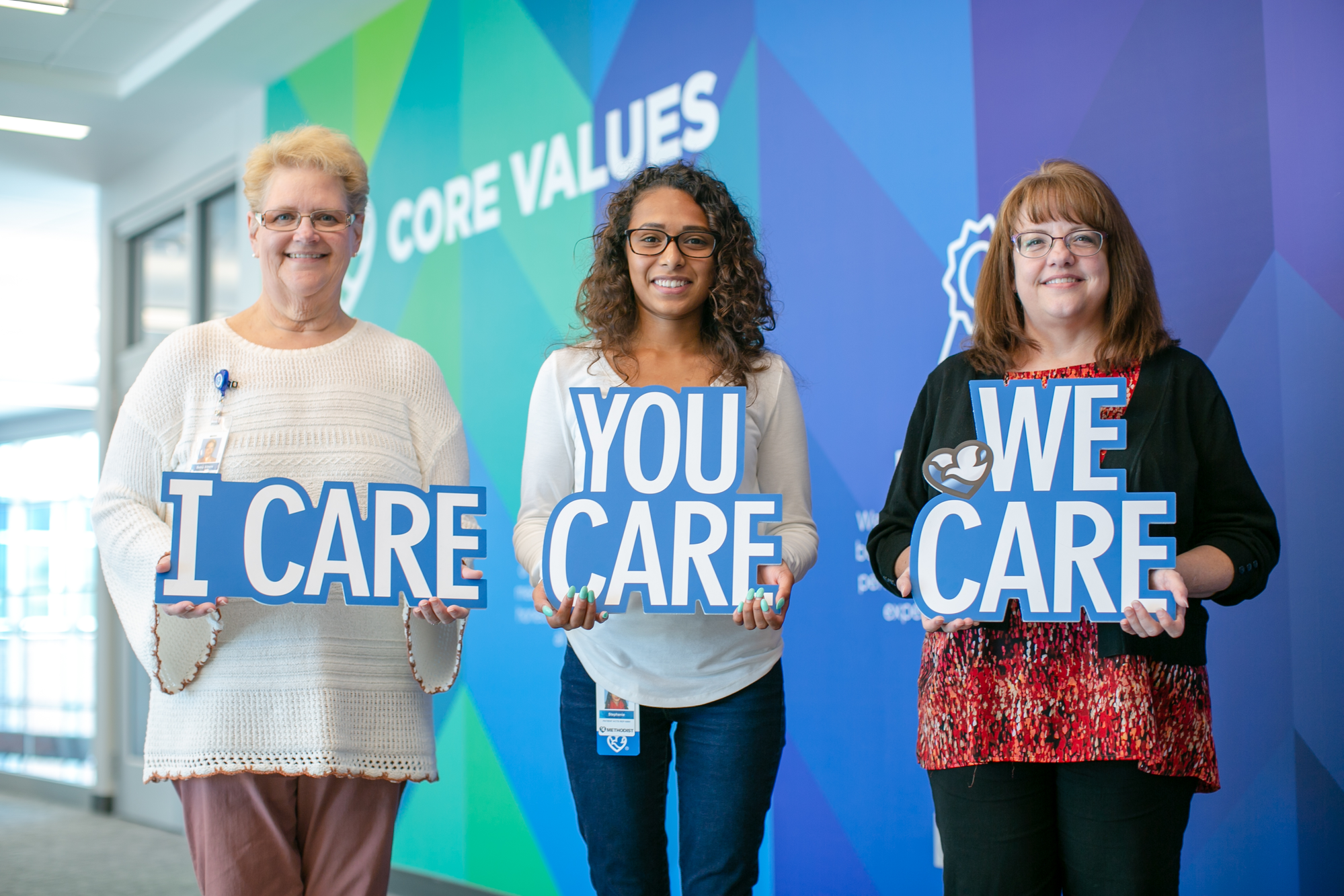 Three Methodist Employees holding signs that spell out the Methodist Caring Campaign slogan